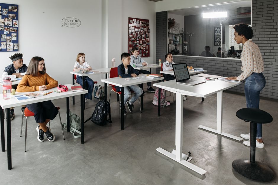 A diverse group of students attentively listens to a teacher in a modern classroom setting.